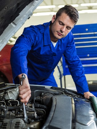 Mechanic in blue coveralls performing engine repair with wrench under the hood of a vehicle, emphasizing expert engine maintenance services at Route 40 Auto.