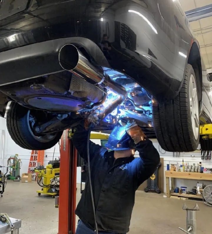 Mechanic performing welding on a vehicle's exhaust system in an auto repair shop, highlighting Route 40 Auto's commitment to thorough diagnostics and reliable repairs.