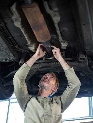 Mechanic inspecting and repairing a vehicle's exhaust system, focusing on the muffler, in an auto repair shop setting, emphasizing exhaust and muffler repair services.