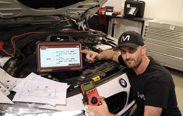Automotive technician performing check engine light diagnostics with OBD-II scanner in a professional auto shop